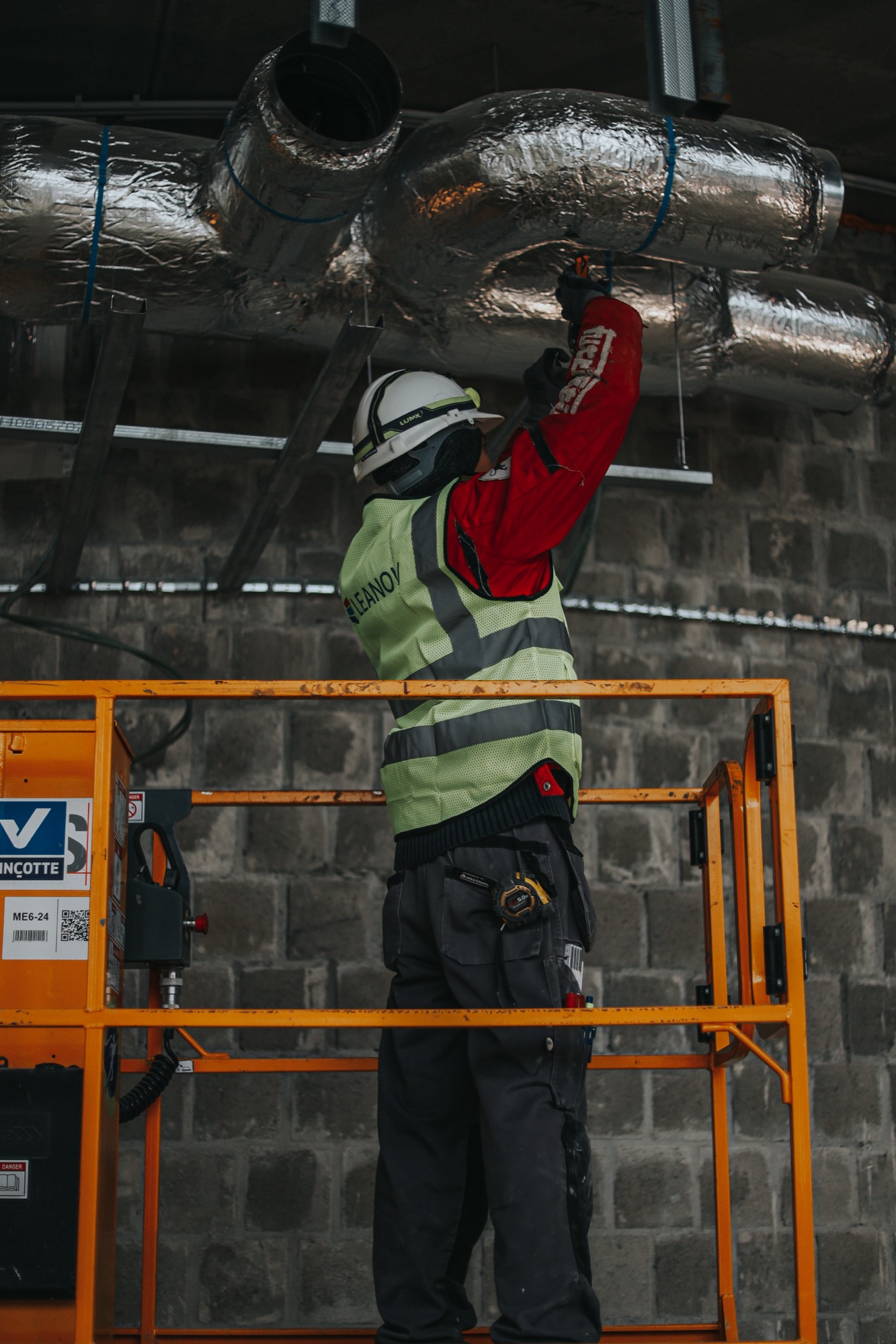 Trabalhador LEANOV em plataforma elevatória a instalar condutas no teto