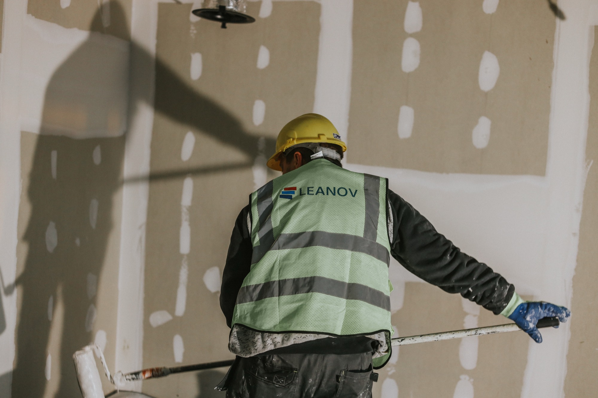 Operário LEANOV a aplicar acabamento numa parede com luz natural
